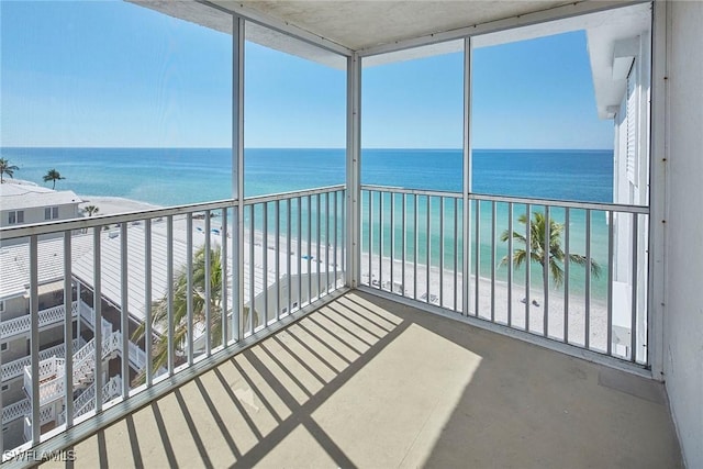 unfurnished sunroom with a water view, a wealth of natural light, and a beach view