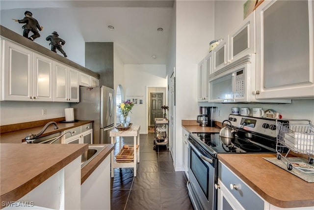 kitchen featuring stainless steel appliances, dark tile patterned flooring, a high ceiling, and white cabinets