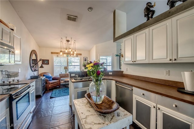 kitchen with appliances with stainless steel finishes, decorative light fixtures, white cabinets, a chandelier, and dark tile patterned floors