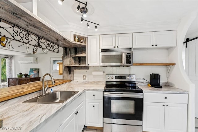 kitchen featuring a barn door, stainless steel appliances, a sink, white cabinets, and an AC wall unit