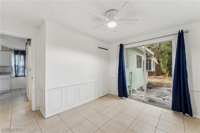 unfurnished room featuring ceiling fan, a wainscoted wall, light tile patterned flooring, and a decorative wall