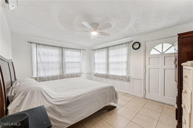 bedroom featuring light tile patterned floors, ceiling fan, and wainscoting