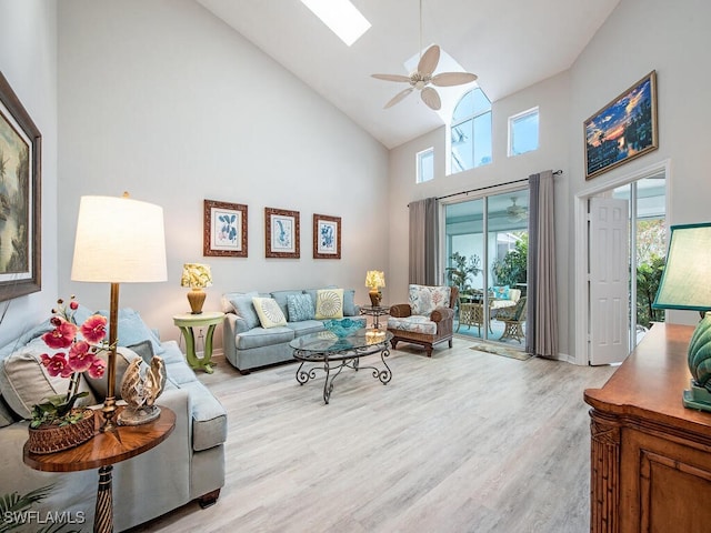 living room with ceiling fan, a skylight, high vaulted ceiling, and light wood-type flooring