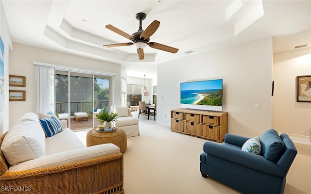 carpeted living room with a raised ceiling and ceiling fan