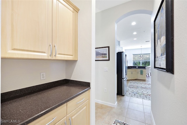 kitchen with light tile patterned floors, stainless steel fridge, light brown cabinetry, and decorative light fixtures