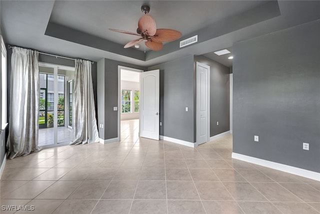 unfurnished room featuring a tray ceiling, ceiling fan, and light tile patterned flooring