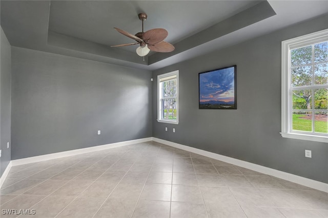 unfurnished room with light tile patterned floors, ceiling fan, and a tray ceiling