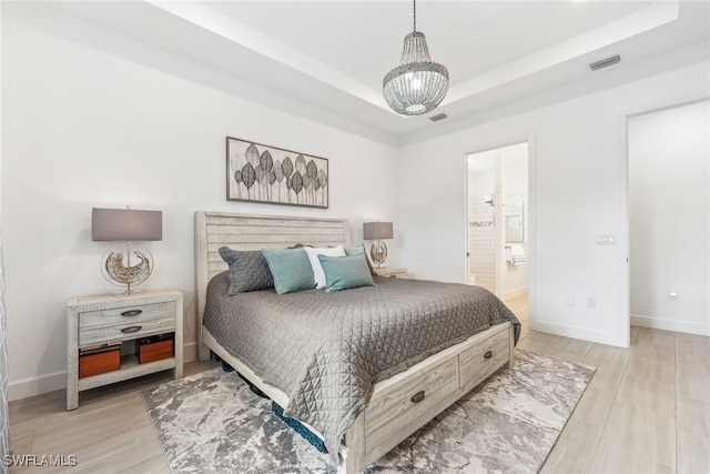 bedroom with a chandelier, ensuite bathroom, a raised ceiling, and light hardwood / wood-style flooring