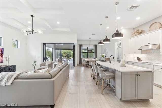 kitchen featuring pendant lighting, backsplash, white cabinetry, and a large island with sink