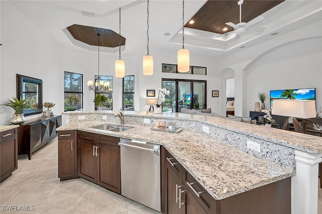 kitchen with a tray ceiling, hanging light fixtures, stainless steel dishwasher, open floor plan, and a sink