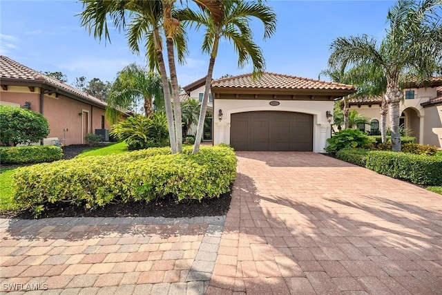 mediterranean / spanish house with a garage, decorative driveway, a tile roof, and stucco siding