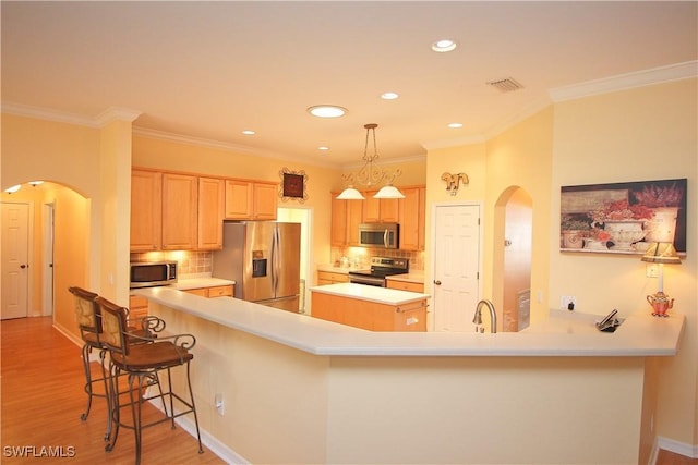 kitchen featuring appliances with stainless steel finishes, kitchen peninsula, a kitchen island, and light brown cabinets