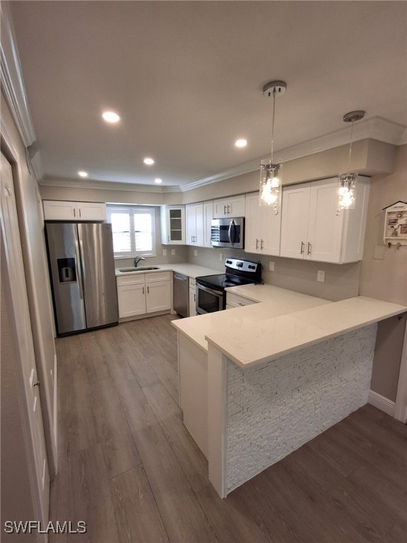 kitchen featuring a peninsula, hanging light fixtures, stainless steel appliances, light countertops, and white cabinetry