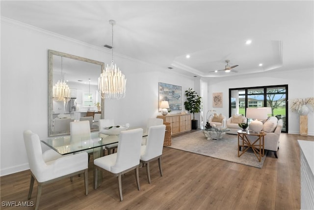 dining room with baseboards, a raised ceiling, wood finished floors, crown molding, and recessed lighting