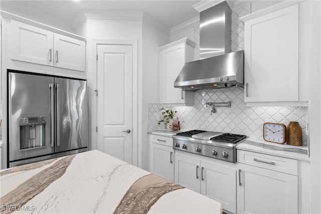 kitchen with wall chimney range hood, white cabinetry, stainless steel appliances, tasteful backsplash, and ornamental molding