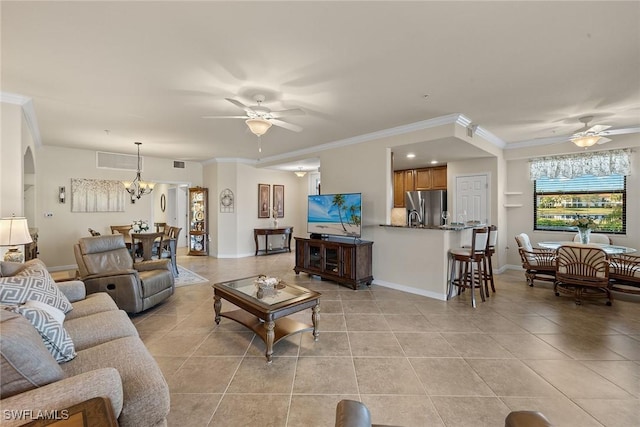 living area featuring light tile patterned floors, arched walkways, ornamental molding, and ceiling fan with notable chandelier