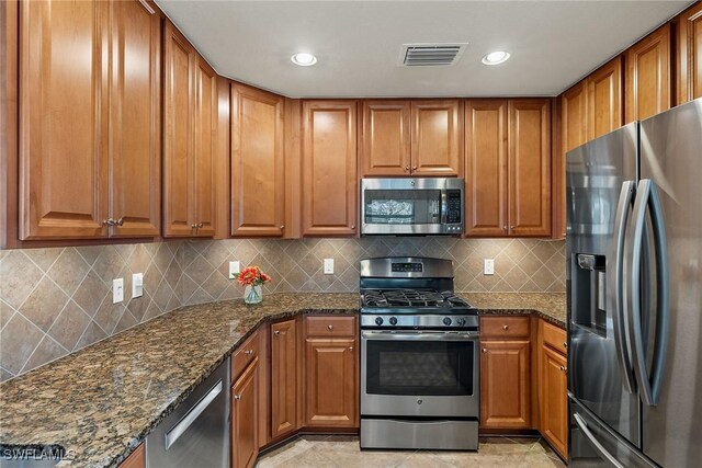 kitchen featuring appliances with stainless steel finishes, brown cabinets, visible vents, and dark stone countertops