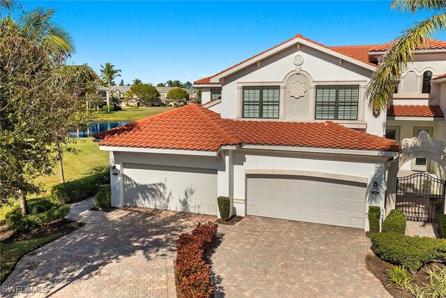 mediterranean / spanish home with a garage, decorative driveway, a tiled roof, and stucco siding