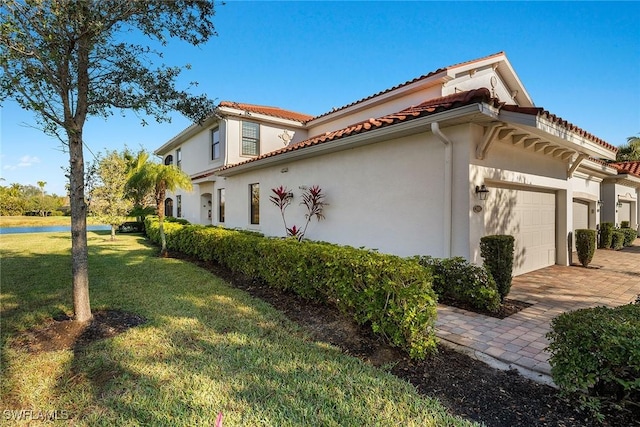 view of side of property featuring a garage, a tiled roof, decorative driveway, a yard, and stucco siding