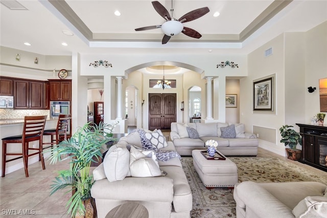 tiled living room with ceiling fan, a tray ceiling, and decorative columns