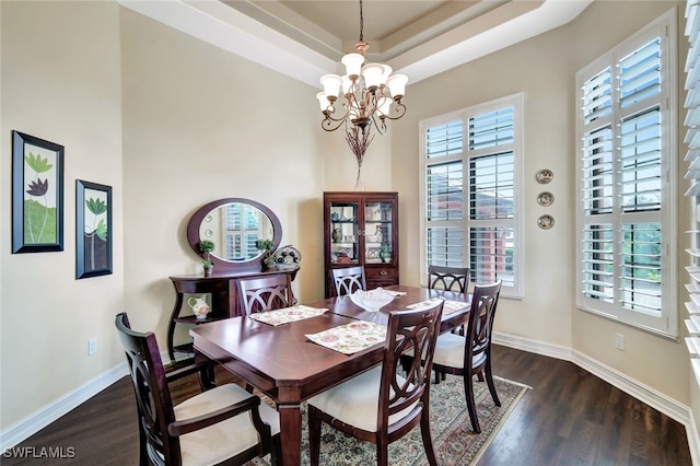 dining room featuring a high ceiling, dark hardwood / wood-style floors, an inviting chandelier, and a raised ceiling