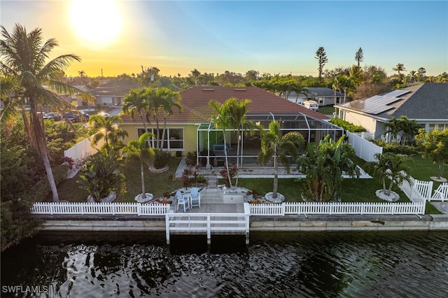 back house at dusk with a water view, a patio, and a lanai