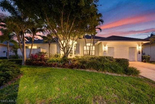 view of front of home featuring decorative driveway, an attached garage, a lawn, and stucco siding