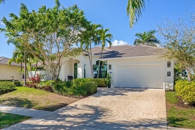 view of front facade featuring decorative driveway, a tiled roof, an attached garage, and stucco siding