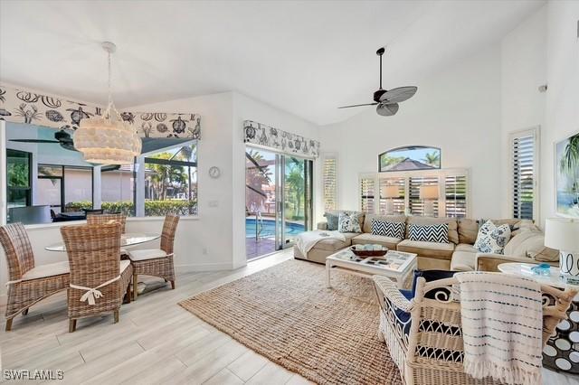 living room featuring baseboards, ceiling fan, high vaulted ceiling, and wood finished floors