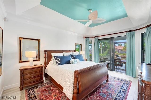 bedroom featuring wood finished floors, a ceiling fan, baseboards, access to exterior, and a raised ceiling