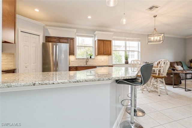 kitchen with light tile patterned floors, light stone counters, hanging light fixtures, and stainless steel fridge