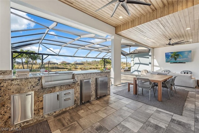 view of patio with ceiling fan, glass enclosure, exterior kitchen, and outdoor dining space