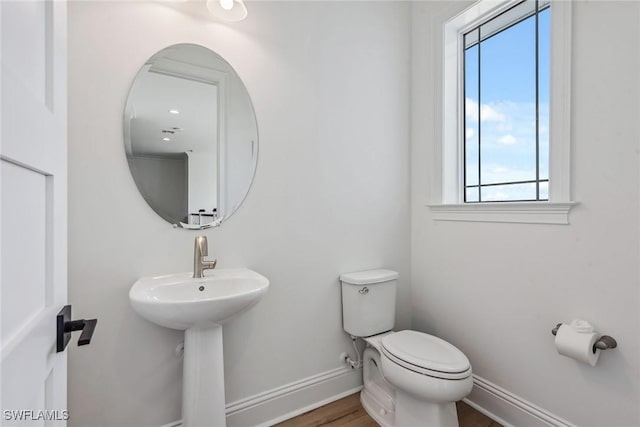 half bathroom with baseboards, a sink, toilet, and wood finished floors