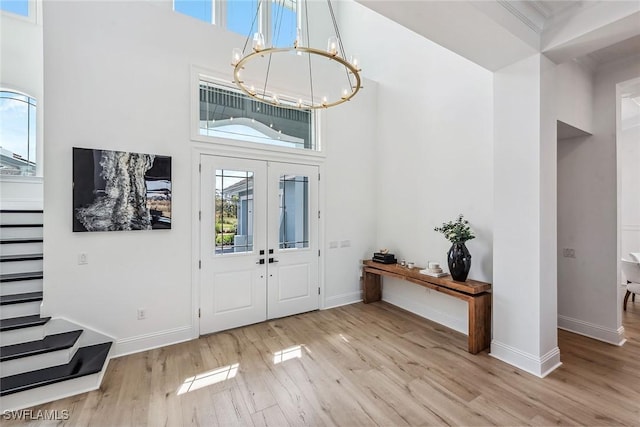 entryway with a notable chandelier, wood finished floors, a towering ceiling, baseboards, and french doors