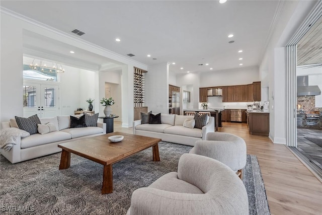 living area with light wood-style floors, recessed lighting, visible vents, and ornamental molding