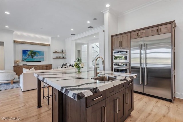 kitchen with light stone counters, stainless steel appliances, a sink, visible vents, and open floor plan