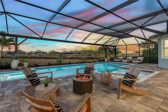 pool at dusk featuring an outdoor pool, glass enclosure, and a patio