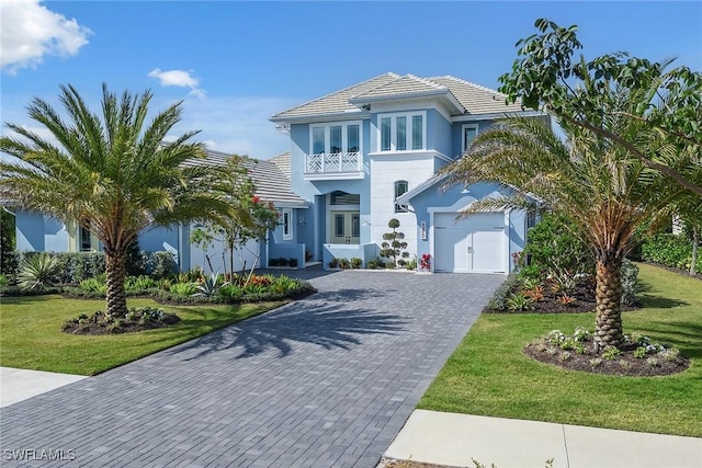 view of front of house featuring an attached garage, decorative driveway, a front yard, and a balcony