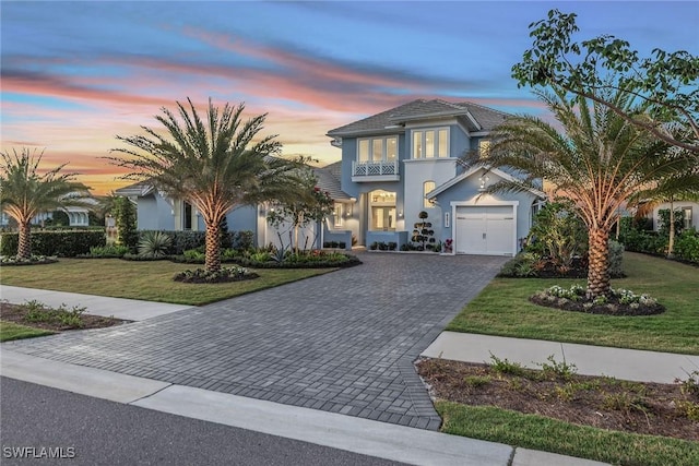 mediterranean / spanish home featuring decorative driveway, a lawn, an attached garage, and stucco siding