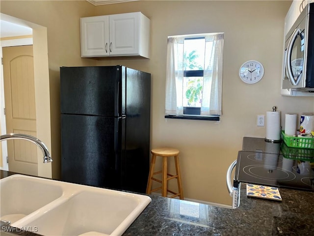 kitchen with stainless steel appliances, white cabinetry, sink, and dark stone countertops