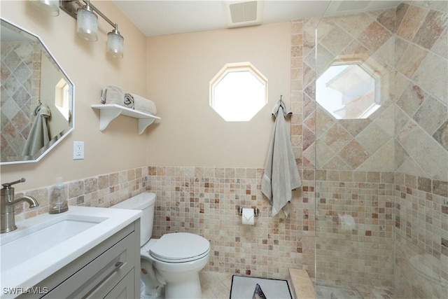 bathroom featuring toilet, visible vents, vanity, tile walls, and wainscoting