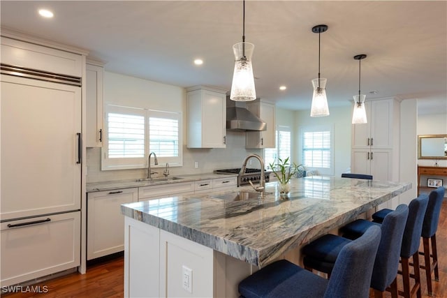 kitchen with wall chimney range hood, paneled refrigerator, a wealth of natural light, and a sink