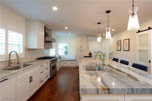 kitchen featuring wall chimney range hood, a barn door, high end range, and a sink