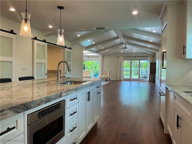 kitchen featuring a barn door, a sink, stainless steel microwave, open floor plan, and vaulted ceiling with beams