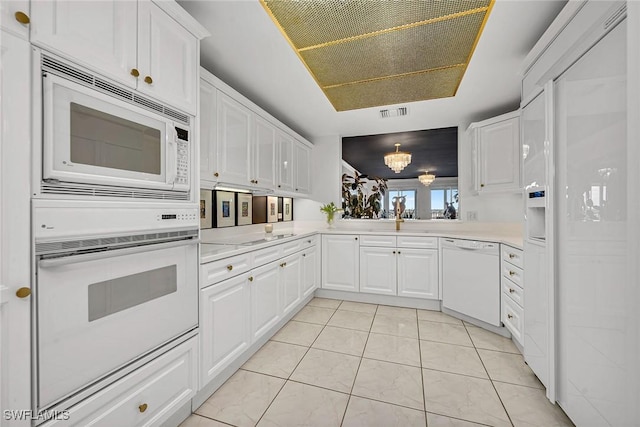 kitchen with light tile patterned floors, white appliances, white cabinetry, an inviting chandelier, and kitchen peninsula