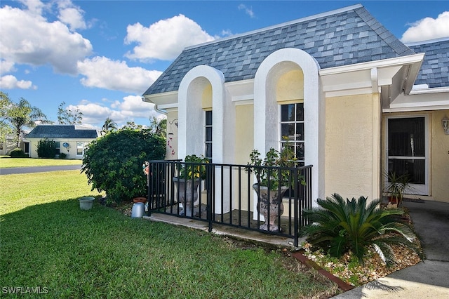 view of home's exterior featuring a shingled roof, mansard roof, a lawn, and stucco siding