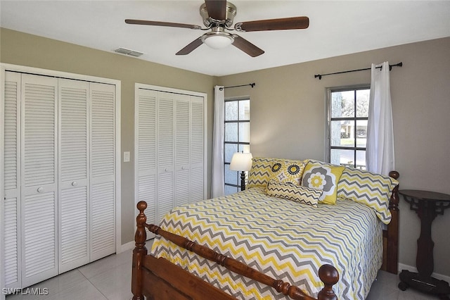 bedroom with ceiling fan, tile patterned flooring, visible vents, baseboards, and multiple closets