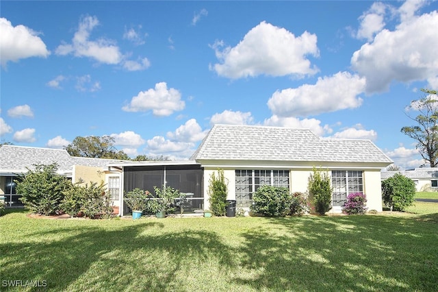 back of house featuring a sunroom, a shingled roof, and a lawn