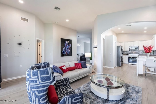 living room featuring arched walkways, light wood-style flooring, visible vents, and recessed lighting