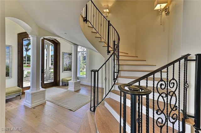 entryway with baseboards, stairs, decorative columns, light wood-style flooring, and arched walkways